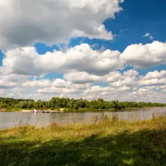 Szeroka Wisła, zielone brzegi i prom. Idealne miejsce na przejażdżkę wiślaną trasą rowerową pod błękitnym niebem z białymi chmurami.