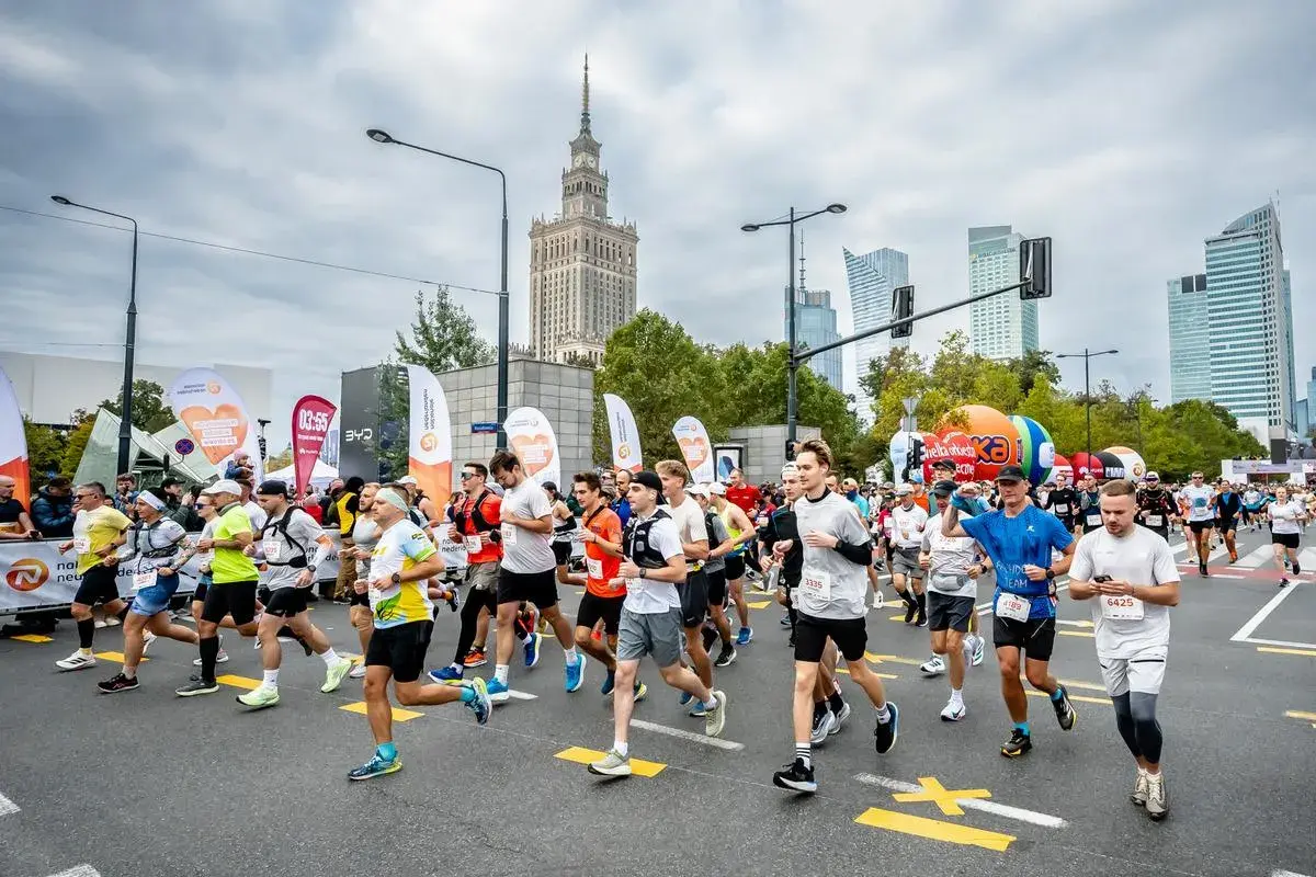 Uczestnicy biegną w maratonie, pokonując dystans 42,195 kilometrów. W tle Pałac Kultury i Nauki.